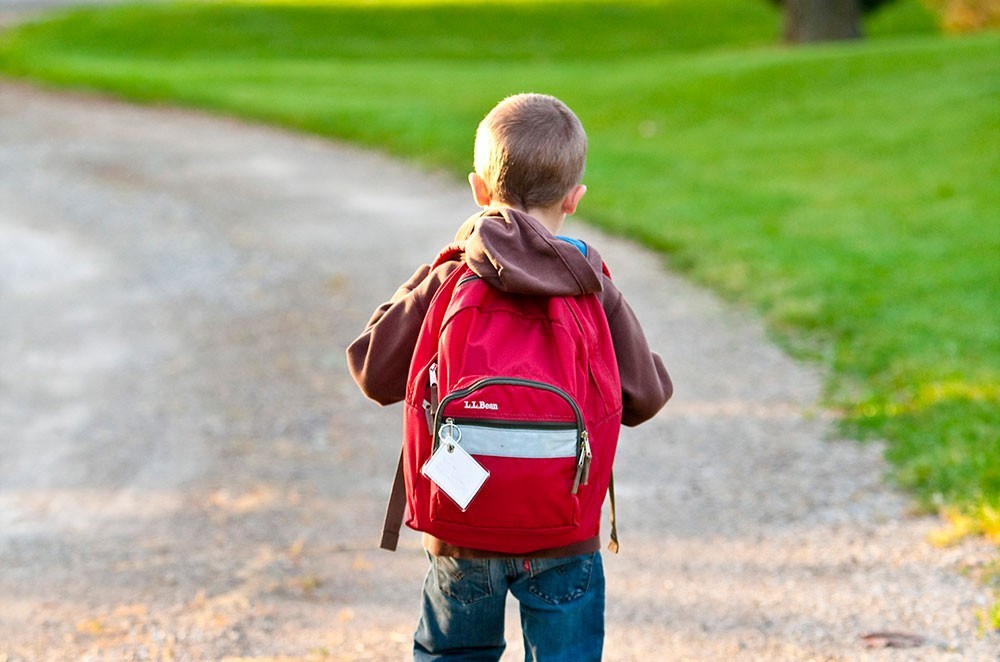 boy in brown hoodie carrying red backpack while walking on 207697