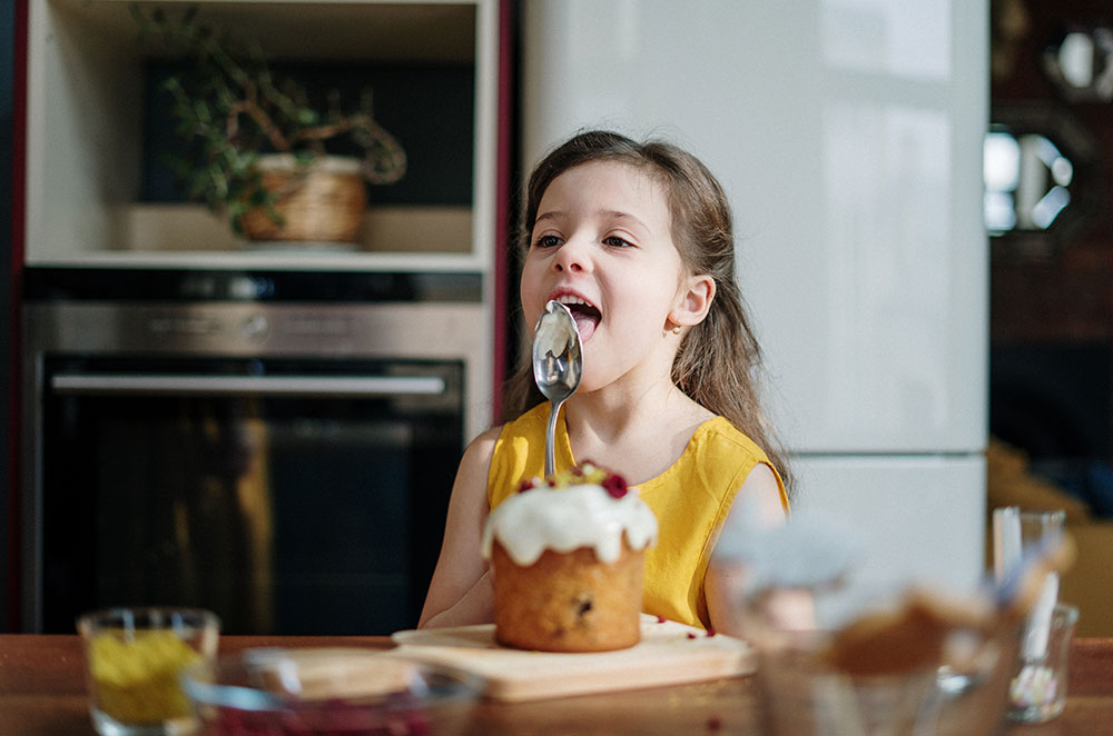 girl in yellow shirt licking icing on spoon 3992388